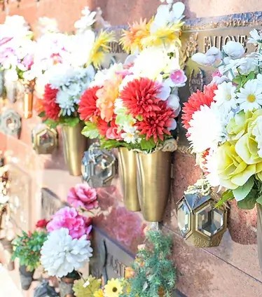 View of crypt from inside cemetery mausoleum featuring various flower arrangements.