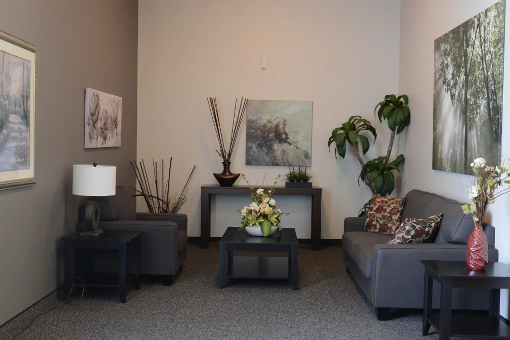 Inside view of cemetery mausoleum, showcasing chairs, flowers, plants, and wall art.