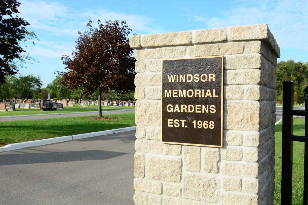 Front entrance to cemetery featuring stone pillar. Metal plaque reads "WINDSOR MEMORIAL GARDENS EST. 1968"